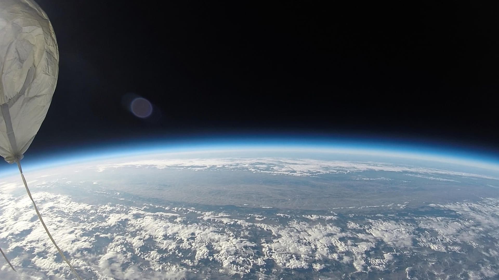 Earth’s curvature and the blackness of space from a weather-balloon camera at the edge of the atmosphere, with the latex balloon in frame.