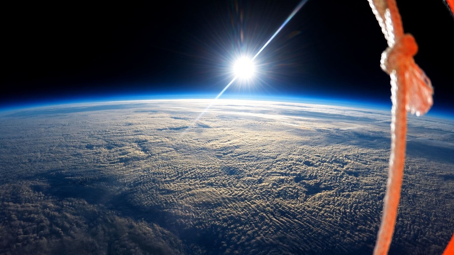 The sun above a curved Earth and a thin blue atmospheric limb, photographed from a high-altitude balloon.